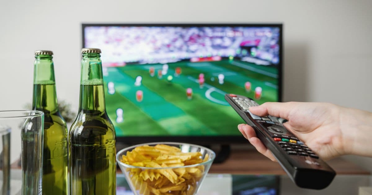 Mano con un mando frente a un televisor con un partido