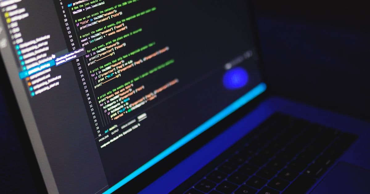 Portátil abierto con código de programación en la pantalla, en una habitación a oscuras
